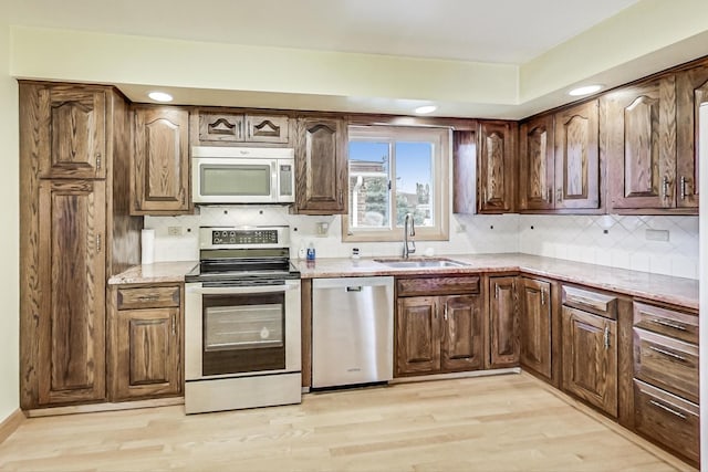 kitchen with light stone counters, a sink, light wood-style floors, appliances with stainless steel finishes, and decorative backsplash