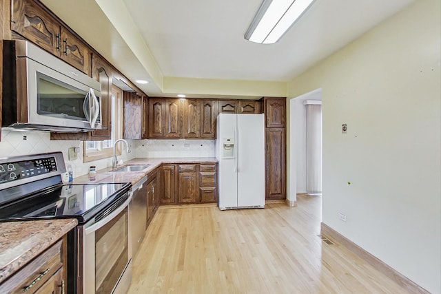 kitchen featuring decorative backsplash, stainless steel appliances, light countertops, light wood-style floors, and a sink