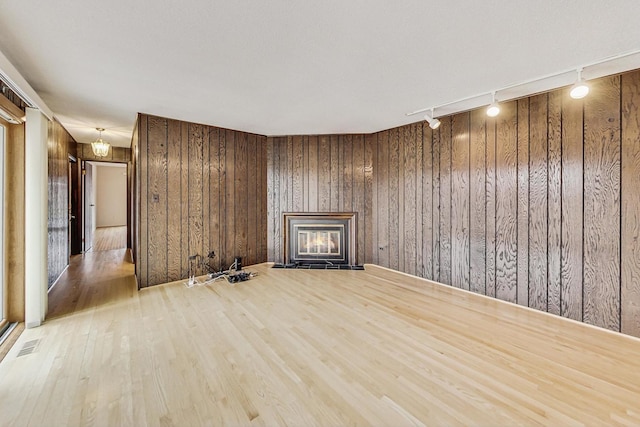 unfurnished living room with visible vents, light wood-style floors, a glass covered fireplace, wood walls, and track lighting