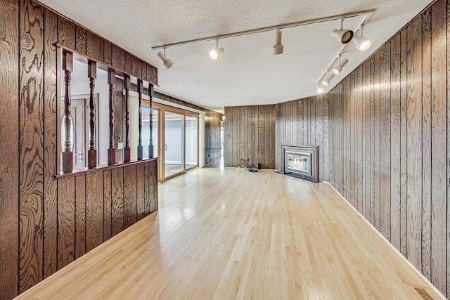 unfurnished living room featuring wood walls, light wood finished floors, a textured ceiling, and a glass covered fireplace