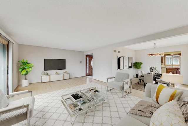 living room with light wood-style floors, visible vents, and an inviting chandelier