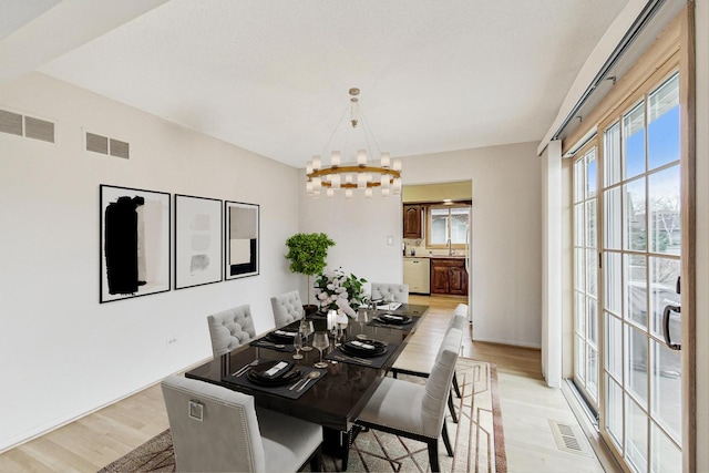 dining room with light wood finished floors, visible vents, and a notable chandelier