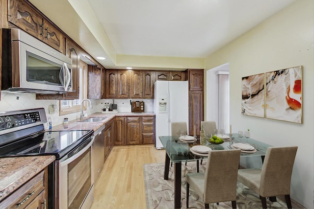 kitchen featuring stainless steel appliances, a sink, light countertops, light wood-type flooring, and tasteful backsplash