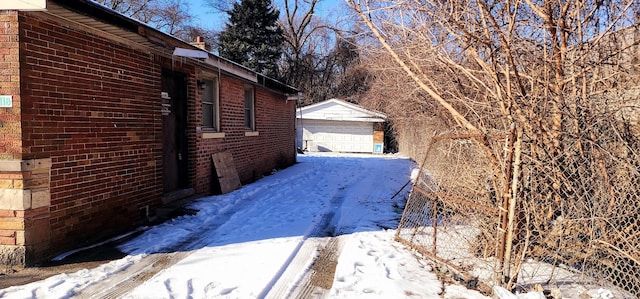 view of snowy exterior with an outbuilding, brick siding, and a garage