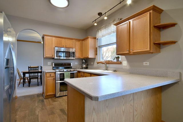 kitchen with kitchen peninsula, stainless steel appliances, light hardwood / wood-style floors, sink, and rail lighting