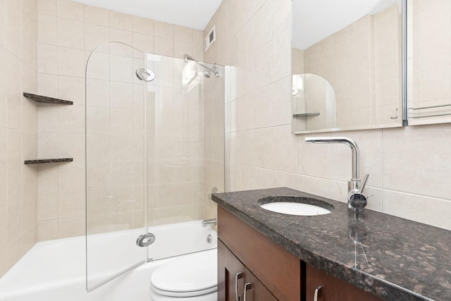 full bathroom featuring toilet, tile walls, combined bath / shower with glass door, tasteful backsplash, and vanity