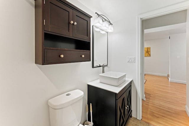 half bathroom with vanity, toilet, wood finished floors, and baseboards