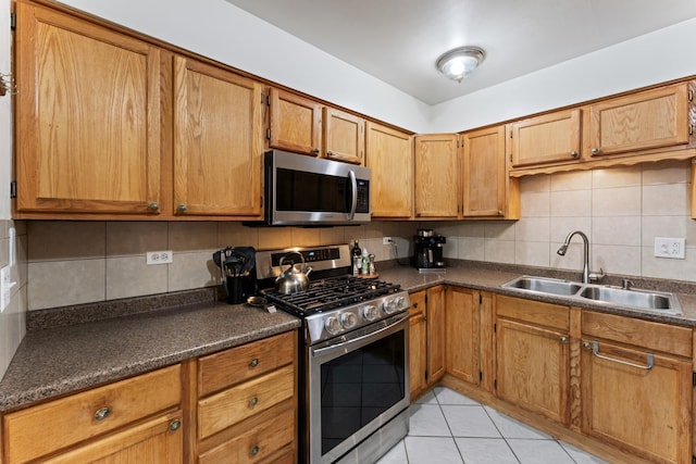 kitchen featuring light tile patterned floors, a sink, appliances with stainless steel finishes, dark countertops, and backsplash