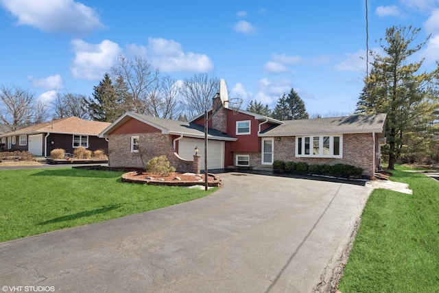 tri-level home with driveway, a chimney, an attached garage, a front yard, and brick siding