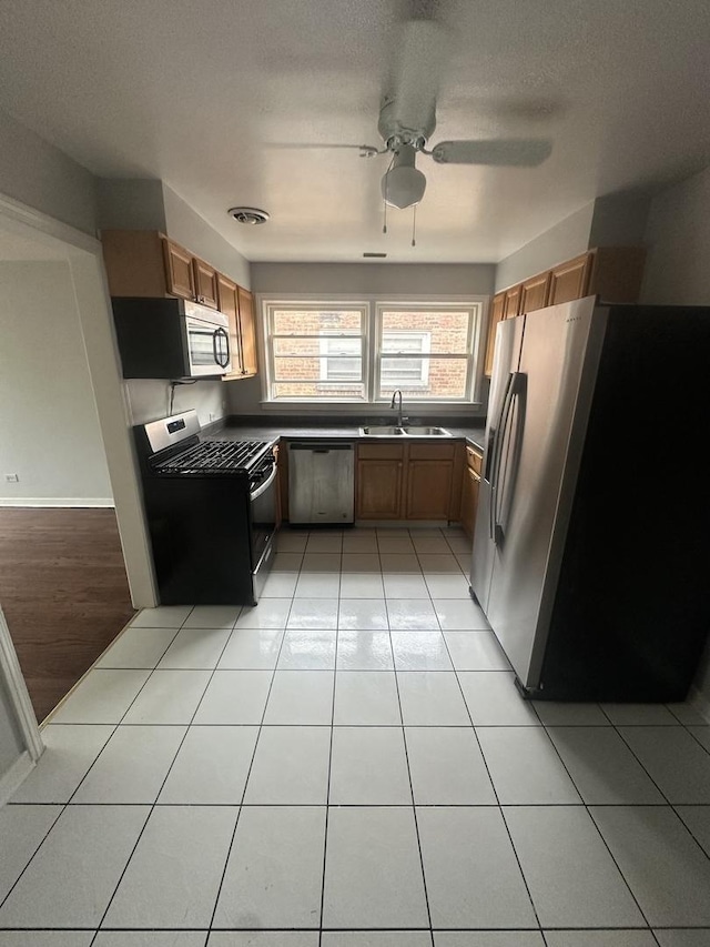 kitchen featuring appliances with stainless steel finishes, brown cabinetry, a sink, and light tile patterned floors