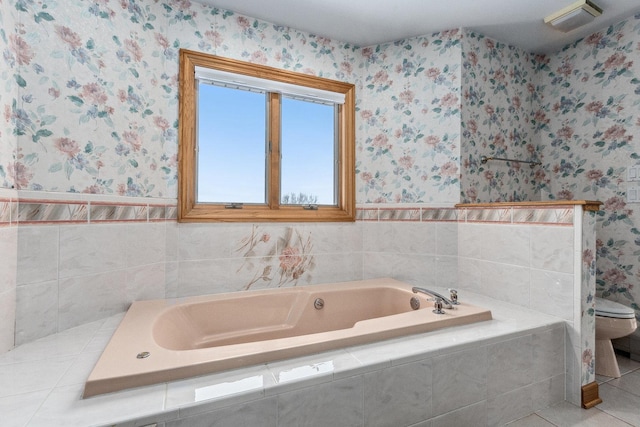 bathroom with tile patterned flooring, toilet, and tiled bath