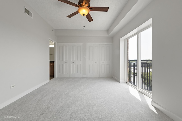 unfurnished bedroom featuring access to exterior, light colored carpet, ceiling fan, and multiple closets