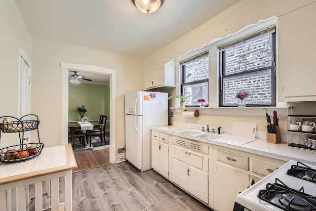 kitchen with white appliances, light countertops, a ceiling fan, light wood-style floors, and a sink