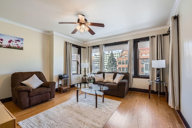 living area with ornamental molding, ceiling fan, light wood-type flooring, and baseboards