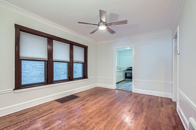 spare room featuring crown molding, a ceiling fan, visible vents, wood finished floors, and baseboards