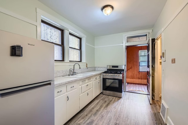 kitchen with stainless steel range with gas stovetop, freestanding refrigerator, light countertops, a sink, and light wood finished floors
