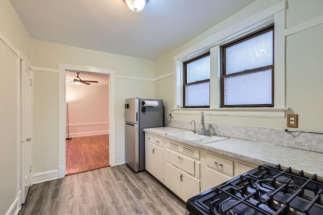 kitchen with light wood-style floors, freestanding refrigerator, black range with gas stovetop, light countertops, and a sink