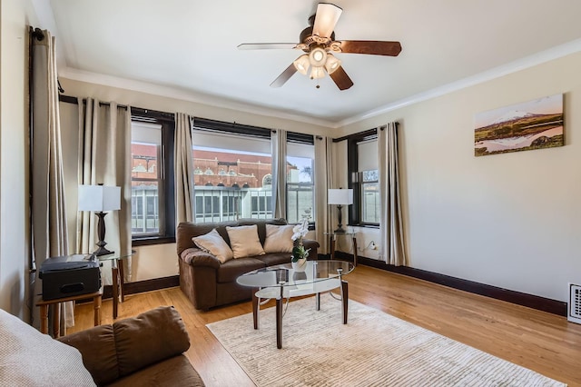 living area featuring visible vents, baseboards, ceiling fan, light wood-style floors, and crown molding