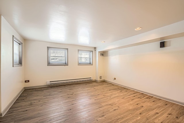 empty room with baseboard heating, wood finished floors, and baseboards