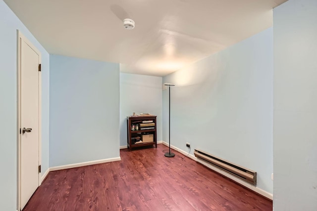 empty room with baseboard heating, wood finished floors, and baseboards