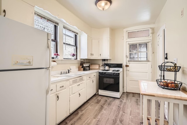 kitchen with white cabinets, a sink, freestanding refrigerator, light wood-style floors, and gas range oven