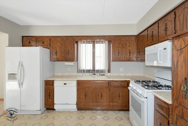 kitchen featuring white appliances, a sink, light countertops, brown cabinets, and light floors