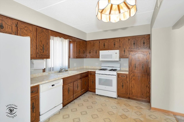 kitchen with brown cabinetry, white appliances, light countertops, and a sink