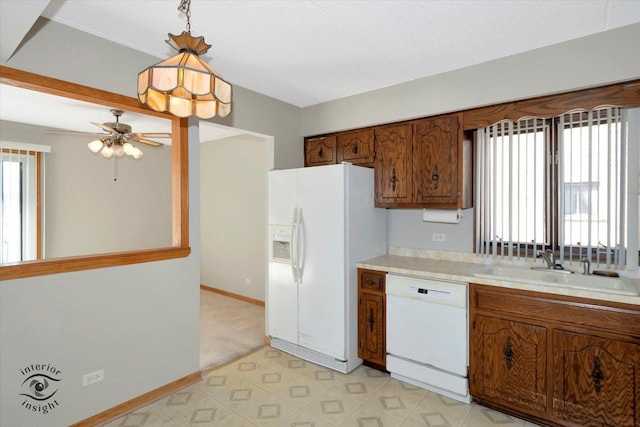 kitchen featuring white appliances, a sink, light countertops, brown cabinets, and decorative light fixtures