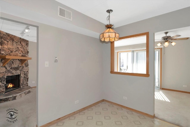 interior space with baseboards, visible vents, light colored carpet, a stone fireplace, and track lighting