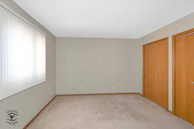 unfurnished bedroom with baseboards, light colored carpet, and multiple closets