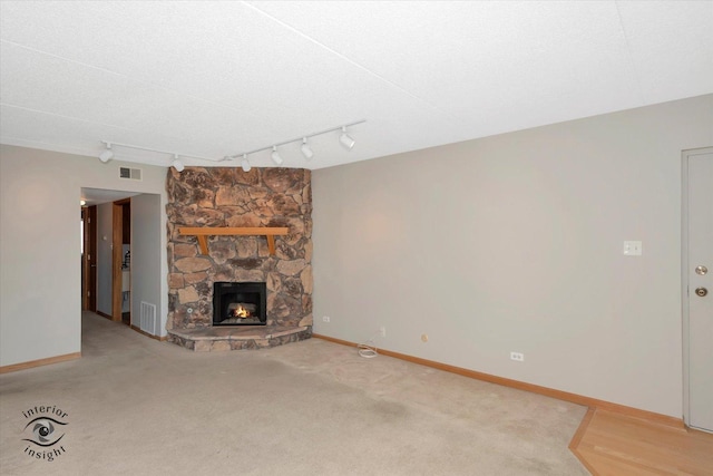 unfurnished living room featuring a stone fireplace, visible vents, and baseboards