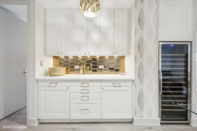 bar featuring light hardwood / wood-style flooring, beverage cooler, white cabinets, hanging light fixtures, and decorative backsplash