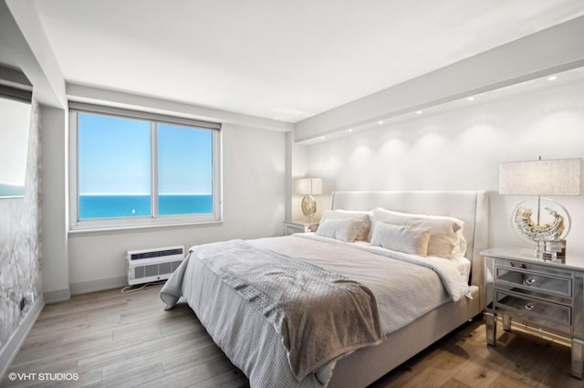 bedroom with a water view, a wall mounted air conditioner, and hardwood / wood-style floors