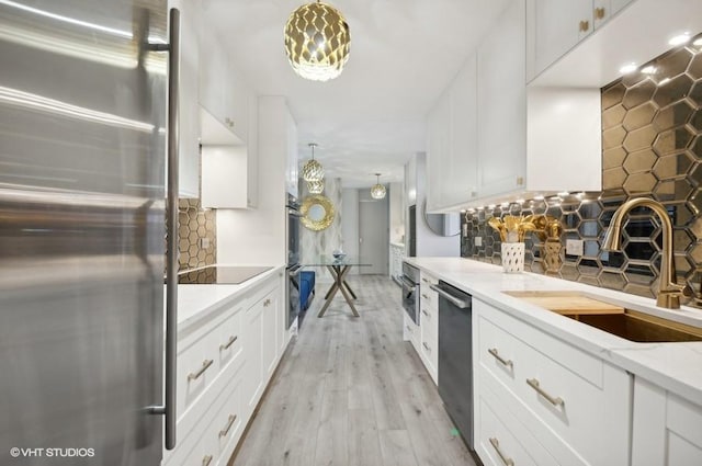 kitchen with tasteful backsplash, white cabinets, pendant lighting, stainless steel refrigerator, and sink