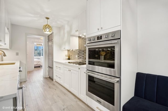 kitchen featuring white cabinetry, stainless steel appliances, decorative light fixtures, light hardwood / wood-style floors, and light stone counters