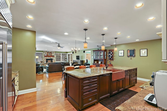 kitchen with built in fridge, a sink, a stone fireplace, and light wood finished floors