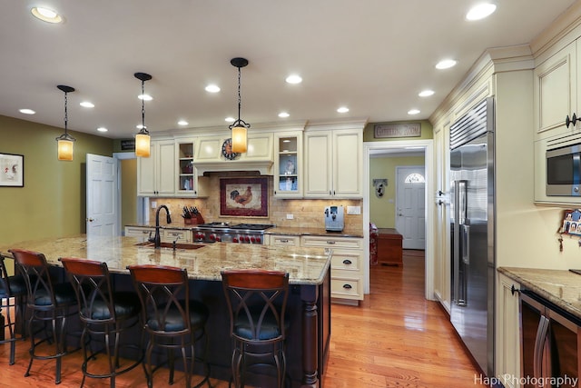 kitchen featuring built in appliances, light stone counters, a sink, light wood-type flooring, and a kitchen bar