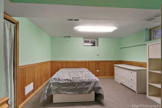 carpeted bedroom with visible vents, a wainscoted wall, and wooden walls