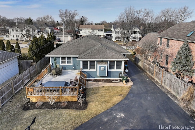 exterior space featuring a deck, aphalt driveway, a shingled roof, fence, and a residential view