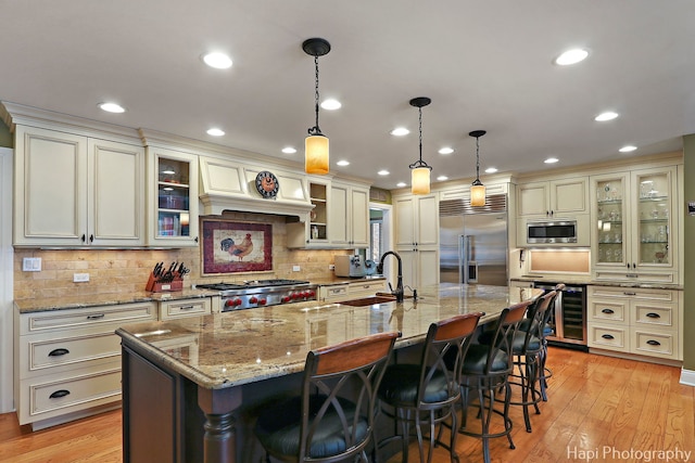 kitchen with built in appliances, beverage cooler, a sink, light wood finished floors, and a center island with sink