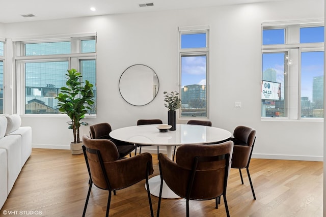 dining area featuring light wood-type flooring, visible vents, baseboards, and a view of city