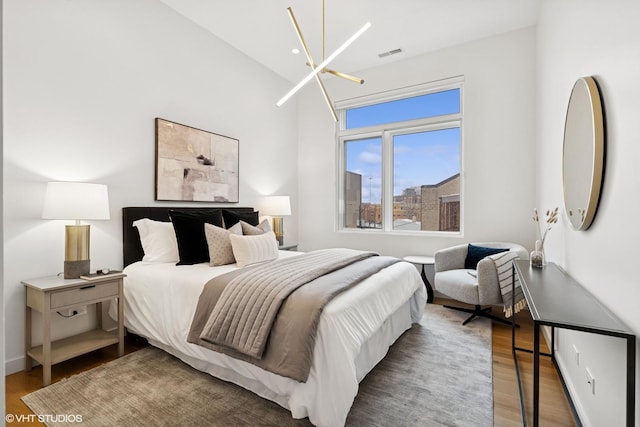 bedroom featuring visible vents, a notable chandelier, baseboards, and wood finished floors