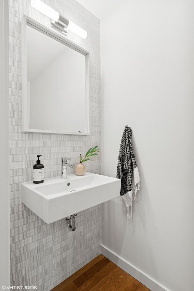 bathroom featuring a sink, backsplash, wood finished floors, and baseboards