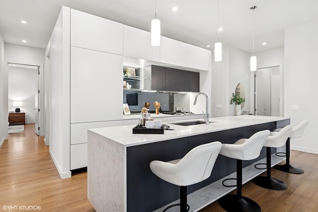 kitchen with light wood-style flooring, white cabinetry, a sink, an island with sink, and modern cabinets