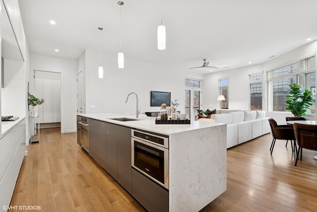 kitchen with light wood-style flooring, a sink, stainless steel oven, open floor plan, and modern cabinets