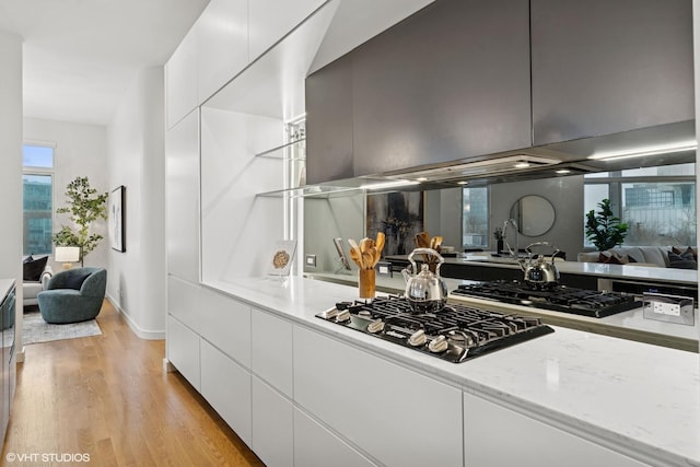 kitchen with light stone counters, gas cooktop, light wood-style flooring, white cabinetry, and modern cabinets