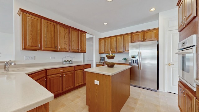 kitchen featuring stainless steel fridge, a kitchen island, oven, light countertops, and a sink