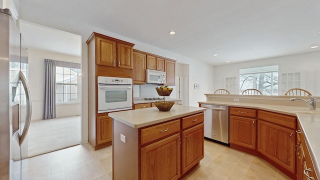 kitchen featuring a center island, stainless steel appliances, light countertops, brown cabinetry, and a sink