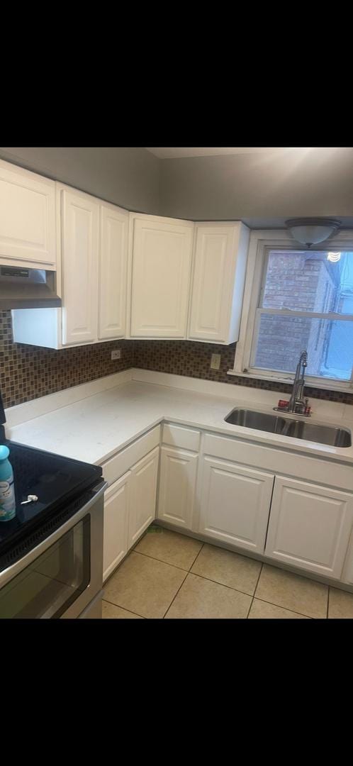 kitchen featuring light tile patterned floors, sink, electric range, white cabinets, and decorative backsplash