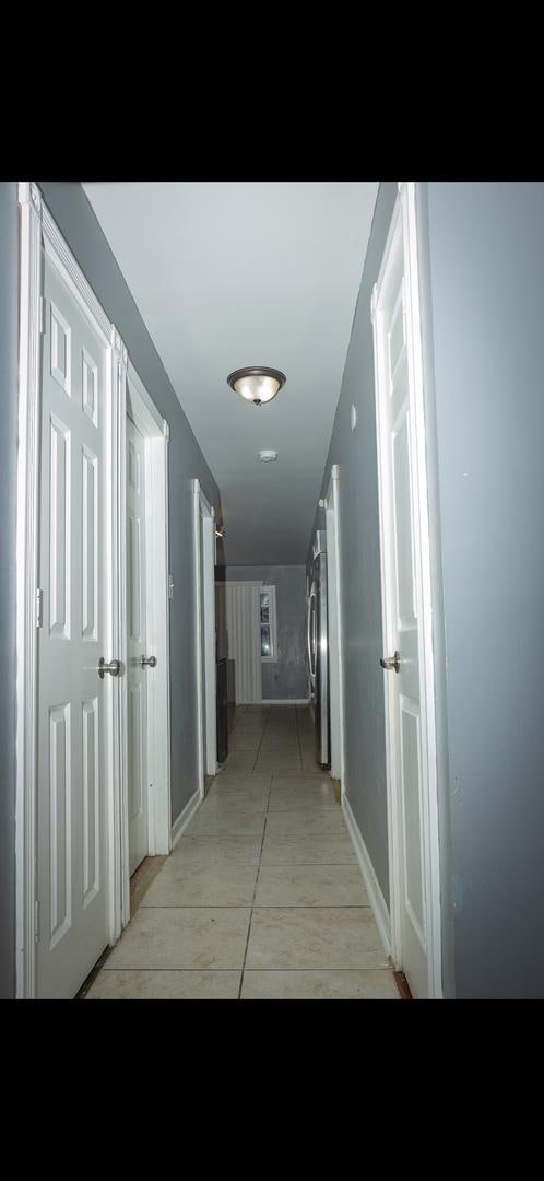 hall featuring stacked washing maching and dryer and light tile patterned flooring